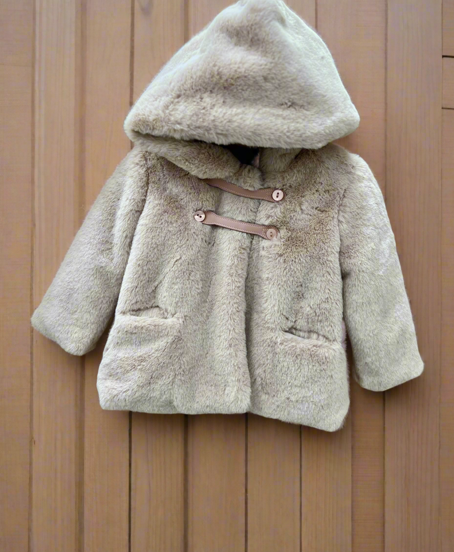 A beige baby girl's fur jacket with a hood, displayed on a wooden surface.