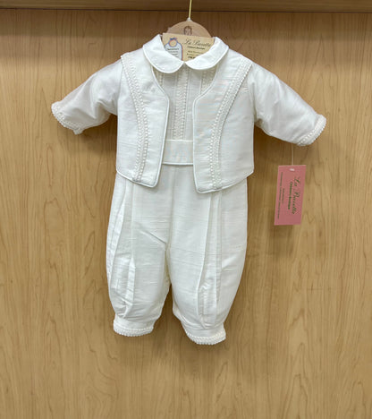 A white silk christening suit for a baby boy, with embellishments such as cording and piping, displayed on a wooden hanger.
