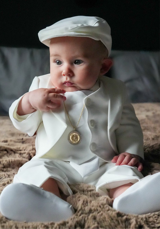 Baby in a white christening wear outfit with a hat sitting on a textured surface