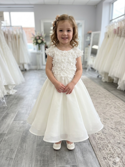 Young girl in a white floral dress standing in a room with wedding dresses.