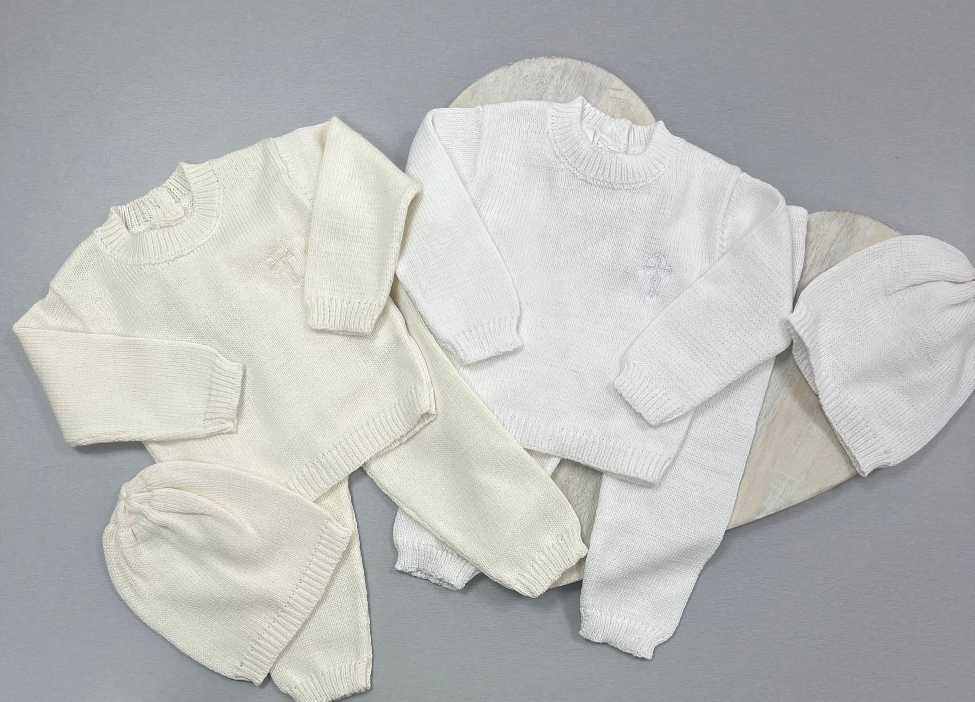 A set of white baby clothes including a long-sleeved top and a beanie hat, displayed on a grey background.
