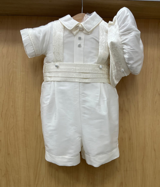 White silk baby shorts christening outfit with jacquard suspenders and a flat cap, displayed on a wooden hanger.