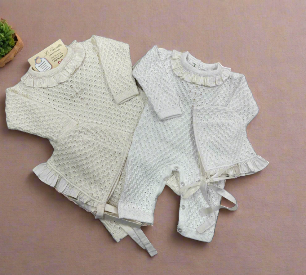 Two beige and white baby girl Christening outfits laid flat, one with a knit pattern and the other a solid color, both with silk ruffles around the neck.