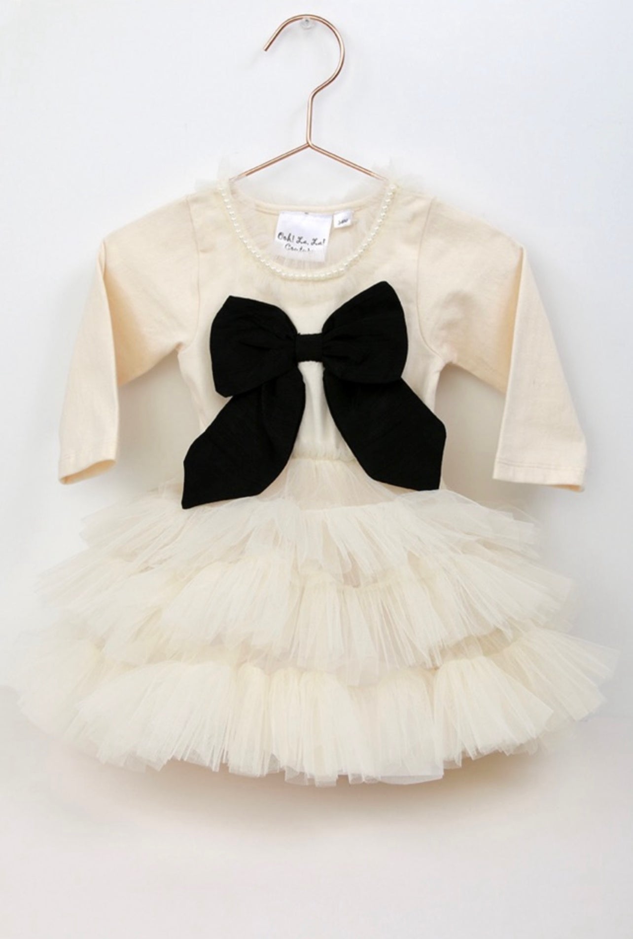 White baby dress with black bow on a hanger against a white background