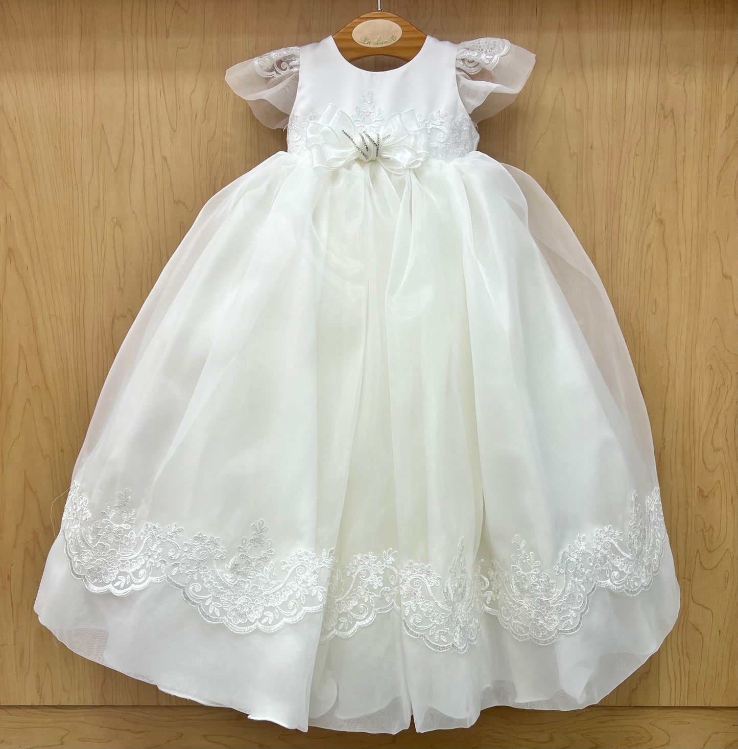 White lace girl Christening dress on a wooden hanger against a wooden background