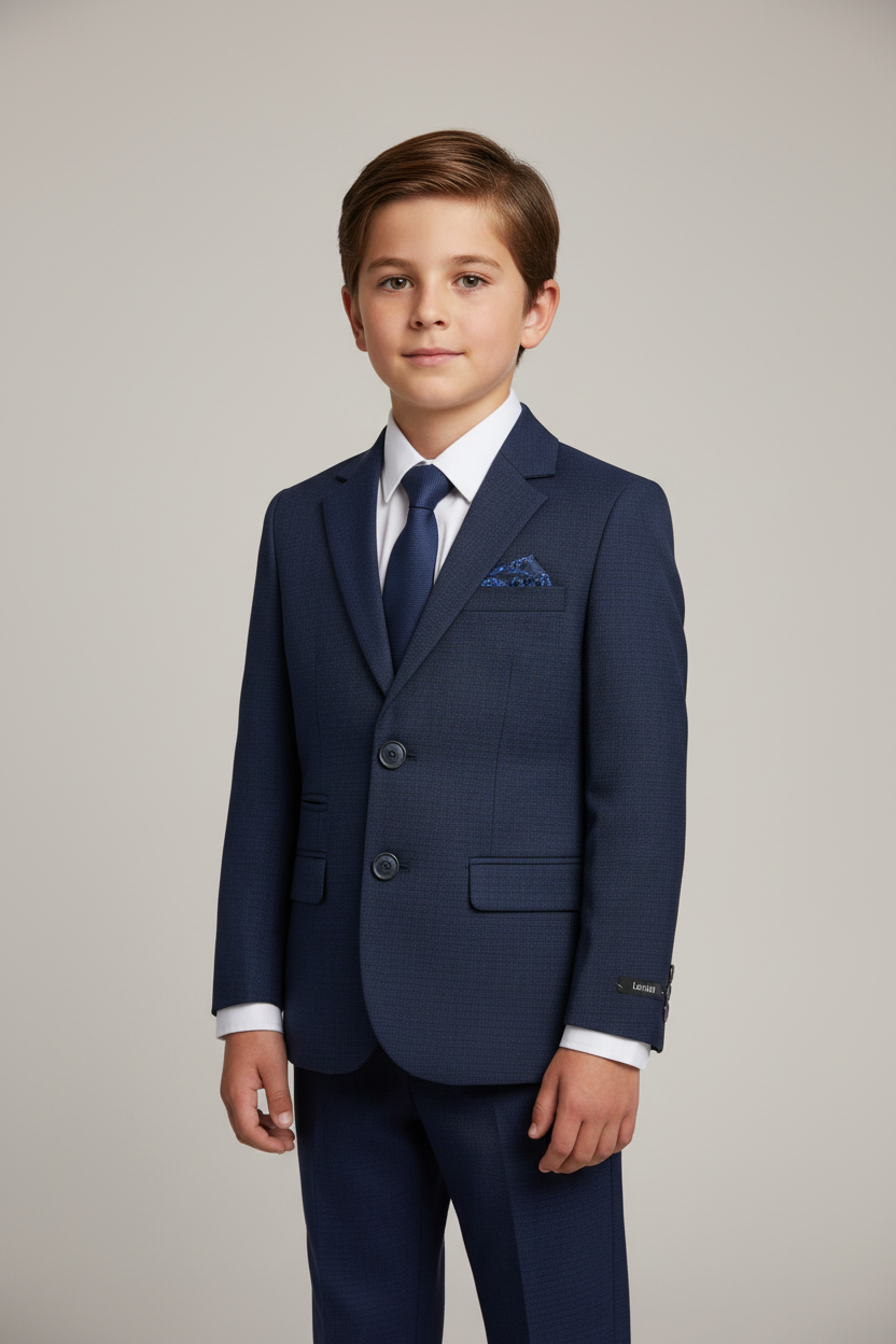 Young boy wearing a navy communion suit with a white shirt and blue tie on a plain background