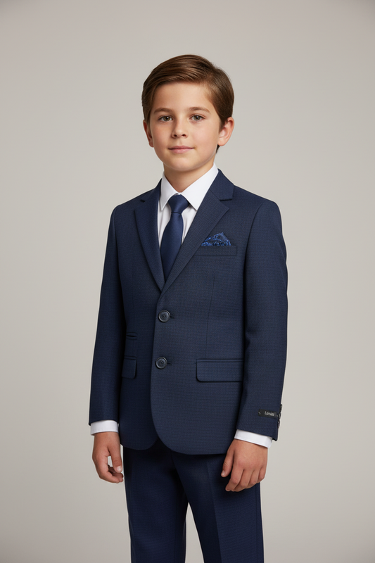Young boy wearing a navy communion suit with a white shirt and blue tie on a plain background