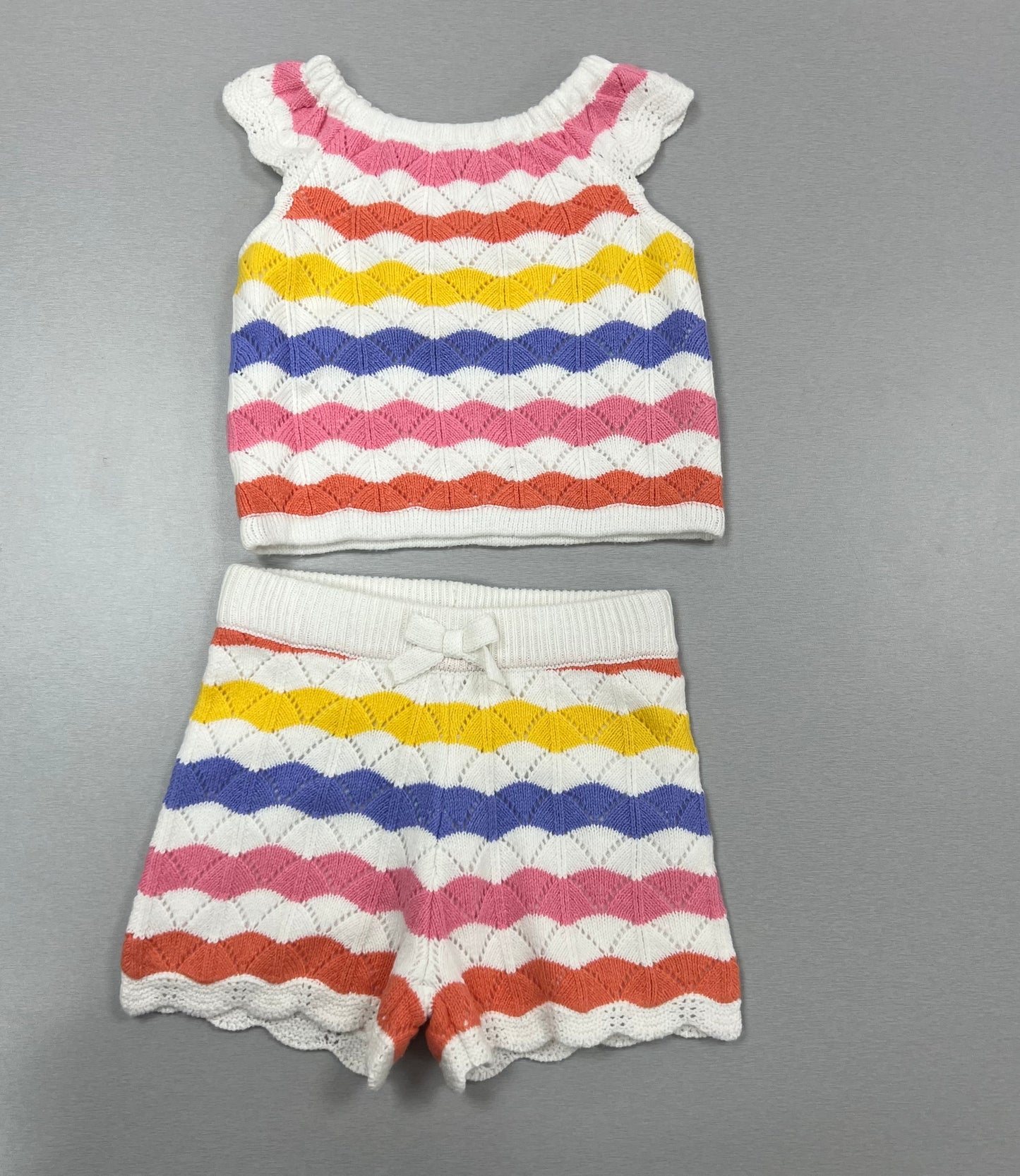 A set of colorful striped crochet shorts and a matching top with scalloped details and a bow on the shorts.